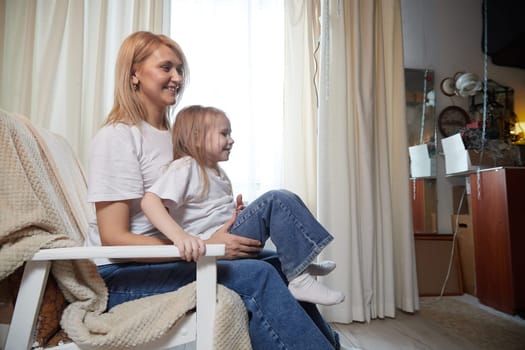 Happy loving family with mother and daughter in living room. Woman mom and small child girl playing and having convercation inside of home