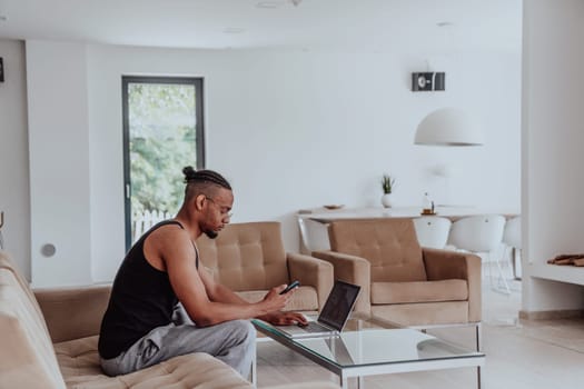 African American man in glasses sitting at a table in a modern living room, using a laptop for business video chat, conversation with friends and entertainment.