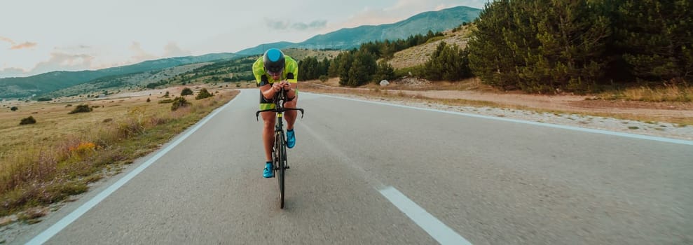 Full length portrait of an active triathlete in sportswear and with a protective helmet riding a bicycle. Selective focus.