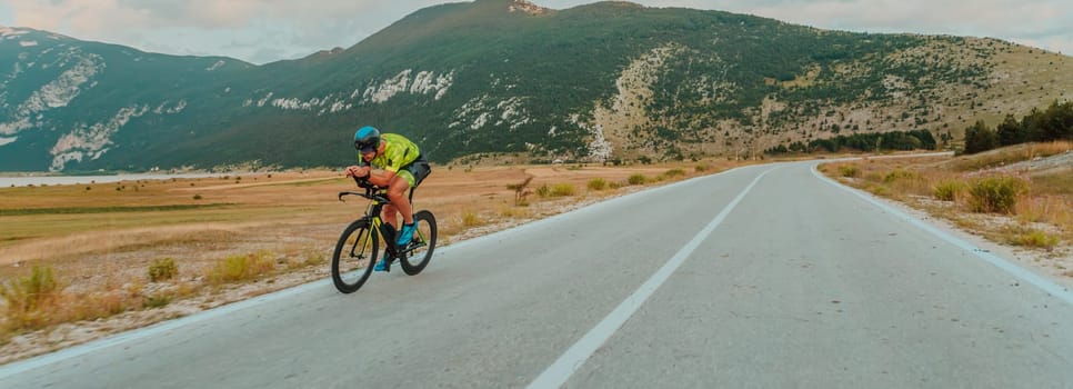 Full length portrait of an active triathlete in sportswear and with a protective helmet riding a bicycle. Selective focus.