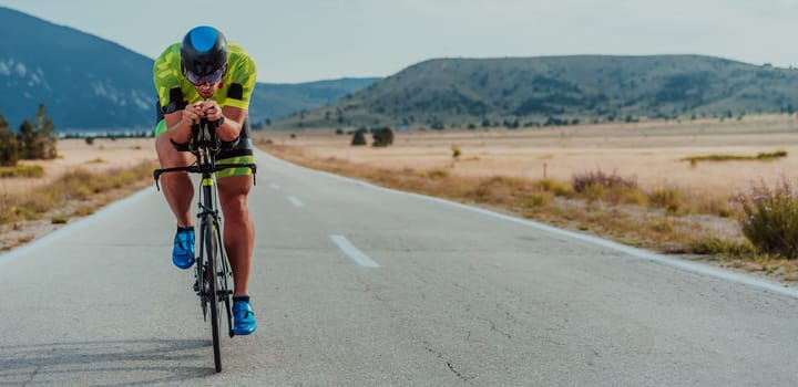 Full length portrait of an active triathlete in sportswear and with a protective helmet riding a bicycle. Selective focus.