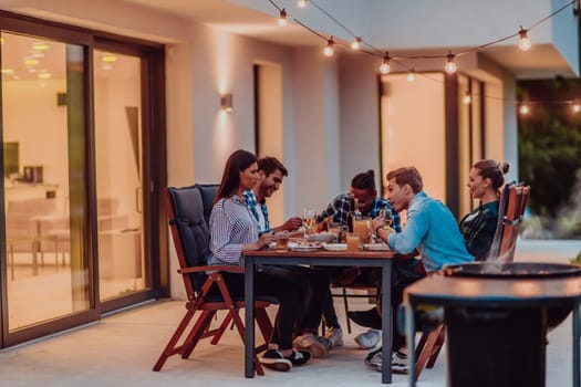 A group of young diverse people having dinner on the terrace of a modern house in the evening. Fun for friends and family. Celebration of holidays, weddings with barbecue