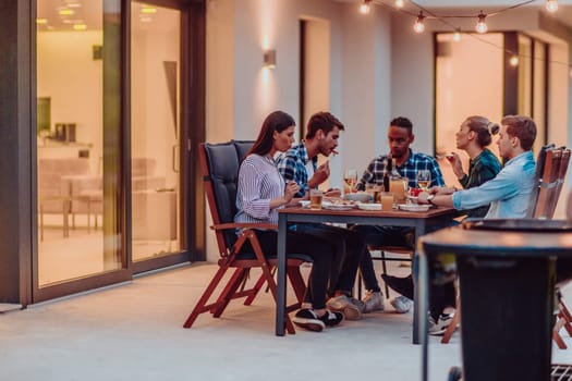 A group of young diverse people having dinner on the terrace of a modern house in the evening. Fun for friends and family. Celebration of holidays, weddings with barbecue