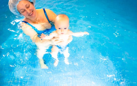 Adorable baby girl enjoying swimming in a pool with her mother early development class for infants teaching children to swim and dive. Swimming instructor doing exercises with a small child in the pool . High quality photo