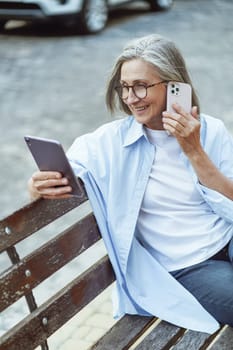 Senior woman searching for information online and speaking on mobile phone. Lady's use of technology to access information and maintain communication while enjoying ambiance of the historic city. . High quality photo