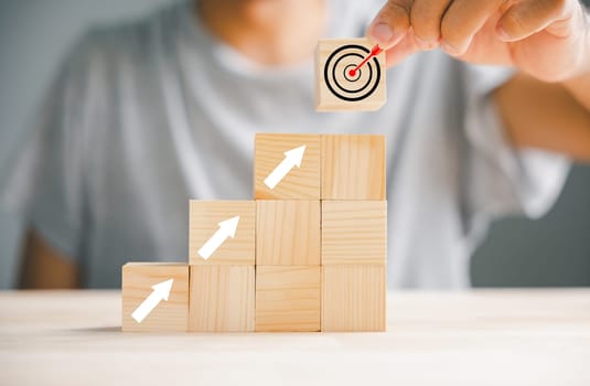 Hand placing a print screen dart and wooden cube on target board with upward arrows. Illustrating the concept of business and investment goals. Isolated on a white background.