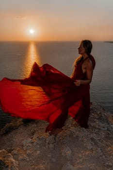 Woman sunset sea red dress, back view a happy beautiful sensual woman in a red long dress posing on a rock high above the sea on sunset