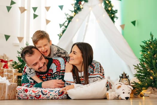 Happy parents play with their little son in a teepee during Christmas holidays, close up