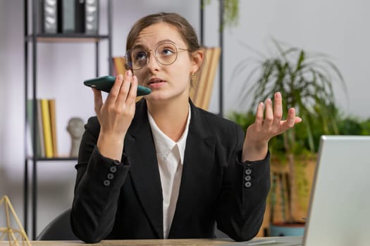 Caucasian young business woman working, having mobile phone loudspeaker talk at office desk with laptop. Manager freelance girl holding smartphone using messenger chat apps. Employment, occupation