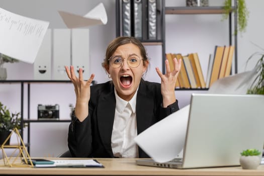 Stressed young business woman working looking at unpaid bank debt bills, doing paperwork, planning budget, calculate finances mortgage payments at office. Displeased freelancer girl throws paper bills