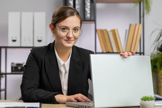 Caucasian young business woman freelancer at office workplace start working on laptop computer. Professional broker freelancer girl opens notebook sends messages makes online purchases watching movies