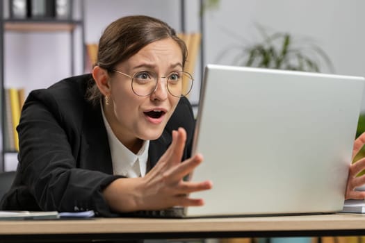 Irritated tired Caucasian business woman while working on laptop, unexpected online website problem, computer virus data loss by hacking. Freelancer feeling mad, broken notebook at office workplace