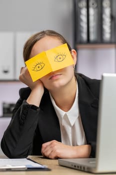 Inefficient tired business woman working sleeping on laptop computer with eyes stickers on face at office workplace desk. Lazy manager freelancer girl. Business people cheating to sleep. Vertical