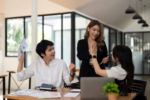 Successful business people giving each other a high five in a meeting. Three young business celebrating teamwork in an office.