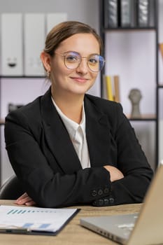 Portrait of happy smiling Caucasian business woman at home office workplace desk looking at camera. Female in formal white shirt. Pretty young girl remote distant online working on laptop. Vertical