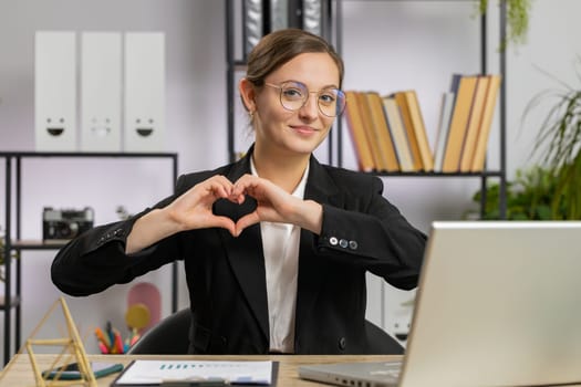 I love you. Caucasian business woman makes symbol of love, showing heart sign to camera, express romantic feelings, express sincere positive feelings at office workplace. Charity, gratitude, donation