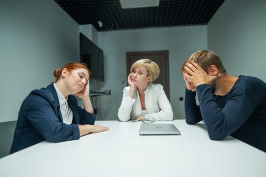 Blond, red-haired woman and bearded man in suits in the office.Colleagues sit at a table in a conference room and hold their heads in thought