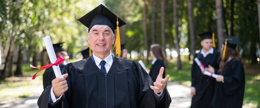 A group of graduates in robes outdoors. An elderly student rejoices at receiving a diploma. Widescreen