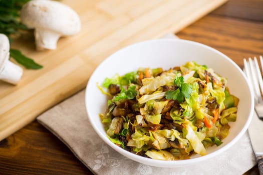 cabbage early fried with mushrooms, carrots and vegetables in a white bowl on a wooden table