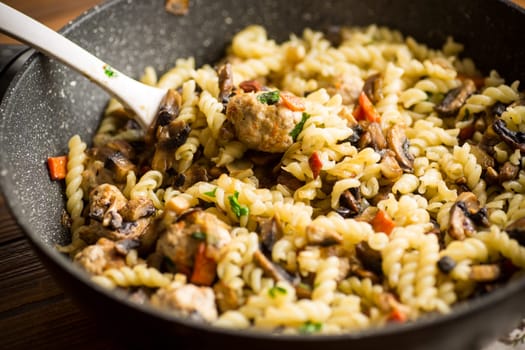 vermicelli cooked with mushrooms, meat and vegetables in a frying pan on a wooden table