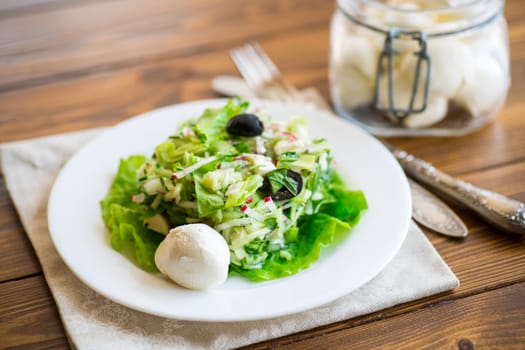 fresh summer salad with early cabbage, cucumbers, radishes and other vegetables in a plate on a wooden table.