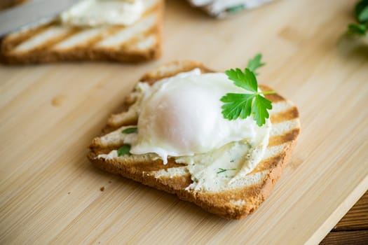 Fried toast bread with spread and poached egg, on a wooden table. Quick breakfast.