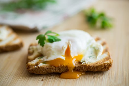 Fried toast bread with spread and poached egg, on a wooden table. Quick breakfast.