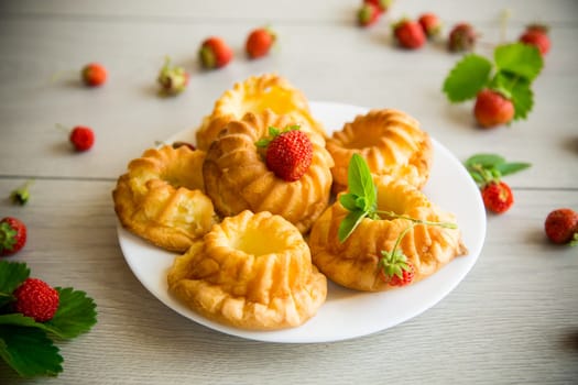 Cooked sweet curd cupcakes with fresh strawberries and mint on a wooden table.