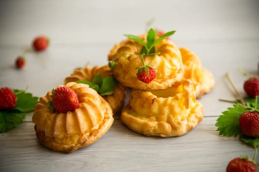 Cooked sweet curd cupcakes with fresh strawberries and mint on a wooden table.