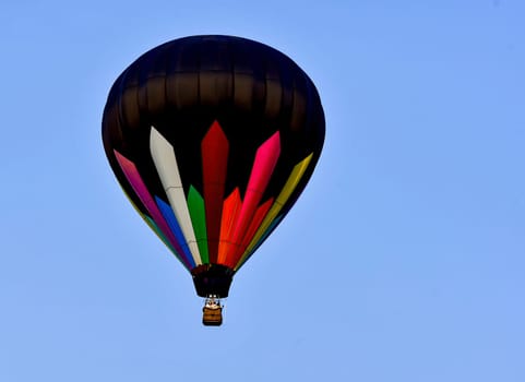 A View of a Hot Air Balloon, Black with Colored Stripes Flying in an all Blue Sky, in Early Fall