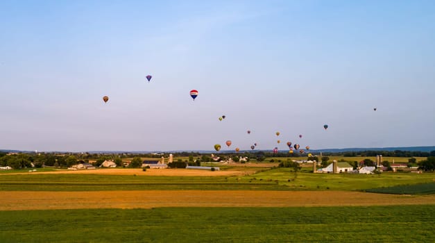 An Drone View of Multiple Colorful Hot Air Balloons Floating Over Farmlands and Countryside on a Beautiful Summer Day, During a Festival