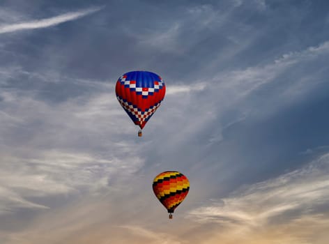 A View of Two Multi Colored Hot Air Balloons Floating in a Beautiful Blue Sky With Thin Clouds