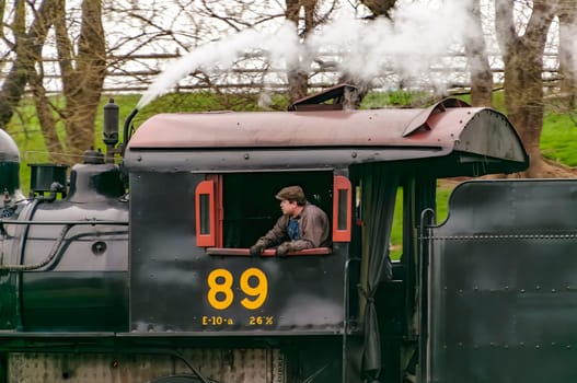 Strasburg, Pennsylvania, April 7, 2023 - A Close Up Side View of a Steam Engines Cab With the Firemen in the Opening as the Train Goes By on a Cloudy Day