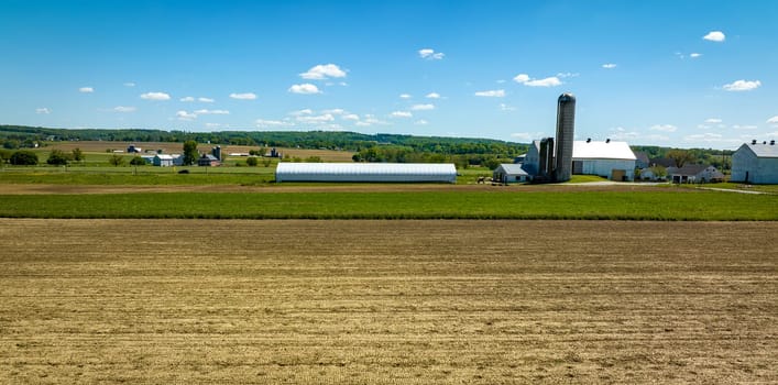 An Aerial View of a Plowed Field with a Barn, Silos and Farm House in View on a Spring Day