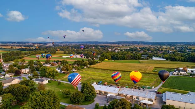 A Drone View of Multiple Colorful Hot Air Balloons Landing in Farms Fields, Parking Lots and Homes on a Beautiful Sunny Summer Afternoon