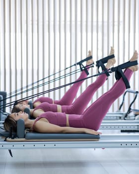 Three Asian women in pink sportswear doing pilates exercises with a reformer bed