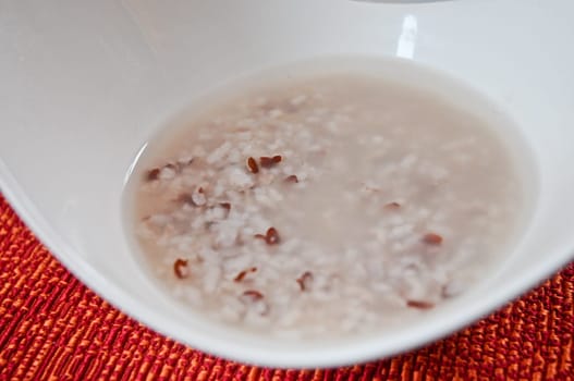 Asian style brown boiled rice in white bowl with lots of watery soup