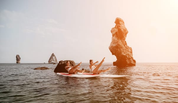 Woman sup yoga. Middle age sporty woman practising yoga pilates on paddle sup surfboard. Female stretching doing workout on sea water. Modern individual hipster outdoor summer sport activity