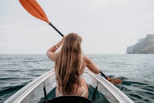 Woman in kayak back view. Happy young woman with long hair floating in transparent kayak on the crystal clear sea. Summer holiday vacation and cheerful female people having fun on the boat.