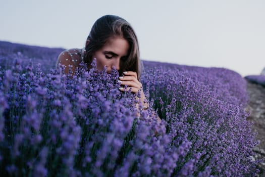 Close up portrait of young beautiful woman in a white dress and a hat is walking in the lavender field and smelling lavender bouquet.