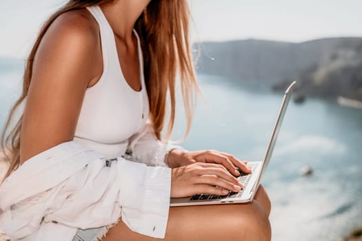 Digital nomad, Business woman working on laptop by the sea. Pretty lady typing on computer by the sea at sunset, makes a business transaction online from a distance. Freelance remote work on vacation