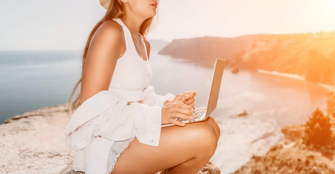 Digital nomad, Business woman working on laptop by the sea. Pretty lady typing on computer by the sea at sunset, makes a business transaction online from a distance. Freelance remote work on vacation