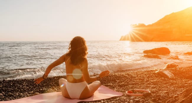 Young woman in swimsuit with long hair practicing stretching outdoors on yoga mat by the sea on a sunny day. Women's yoga fitness pilates routine. Healthy lifestyle, harmony and meditation concept.