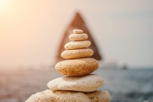 Pyramid stones on the seashore with warm sunset on the sea background. Happy holidays. Pebble beach, calm sea, travel destination. Concept of happy vacation on the sea, meditation, spa, calmness.