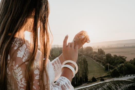 Romantic beautiful bride in white dress posing with sea and mountains in background. Stylish bride standing back on beautiful landscape of sea and mountains on sunset