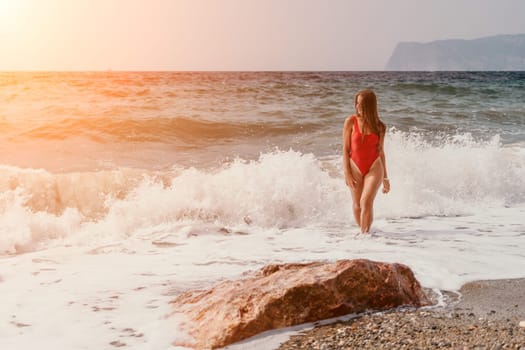 Woman travel sea. Young Happy woman in a long red dress posing on a beach near the sea on background of volcanic rocks, like in Iceland, sharing travel adventure journey