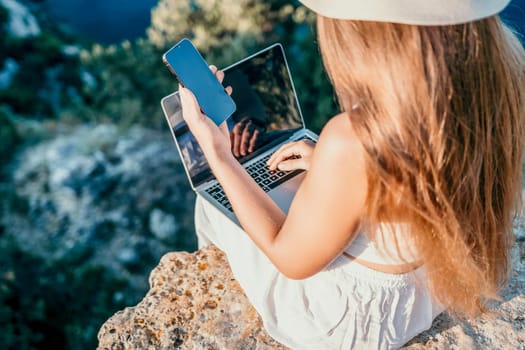 Successful business woman in yellow hat working on laptop by the sea. Pretty lady typing on computer at summer day outdoors. Freelance, travel and holidays concept.