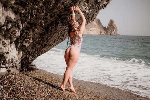 Beach vacation. Hot beautiful woman in sunhat and bikini standing with her arms raised to her head enjoying looking view of beach ocean on hot summer day.