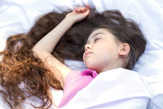 Adorable Little Girl With Extra Long Hair Lying On Sheet, White Linen, Sleeping Under Blanket. Caucasian Asian Brown Haired Child Taking a Rest. Carefree, Happy Childhood, Closeup, Horizontal Plane