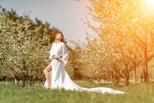 Blond blooming garden. A woman in a white dress walks through a blossoming cherry orchard. Long dress flies to the sides